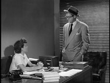 Clark Kent looks at Lois Lane at her desk