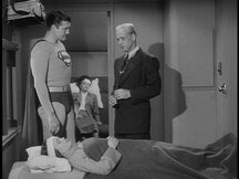 Superman talks with the doctor as the unconscious Maria lies on a bed