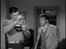 Superman examines the fim strip while Jim looks on